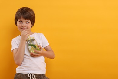 Photo of Cute little boy drinking lemonade on orange background, space for text. Refreshing drink