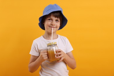 Photo of Cute little boy in panama hat drinking juice on orange background. Refreshing drink