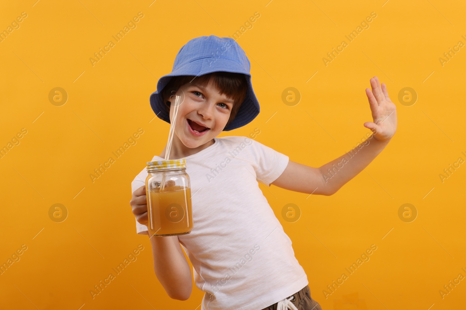 Happy little boy in panama hat with mason jar of juice on orange background. Refreshing drink Photo of Happy little boy in panama hat with mason jar of juice on orange background. Refreshing drink