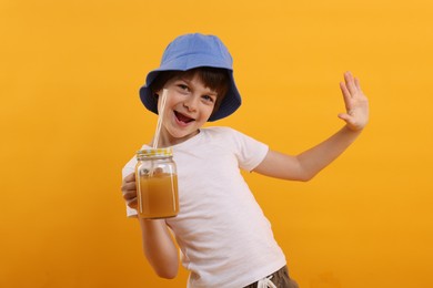 Photo of Happy little boy in panama hat with mason jar of juice on orange background. Refreshing drink