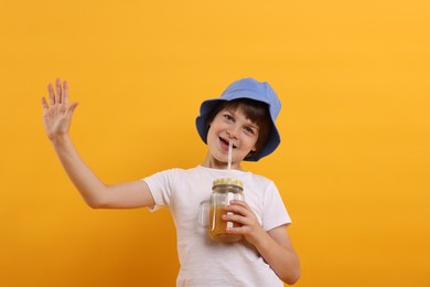 Photo of Happy little boy in panama hat with mason jar of juice on orange background. Refreshing drink