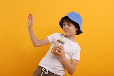 Photo of Cute little boy in panama hat drinking juice on orange background. Refreshing drink