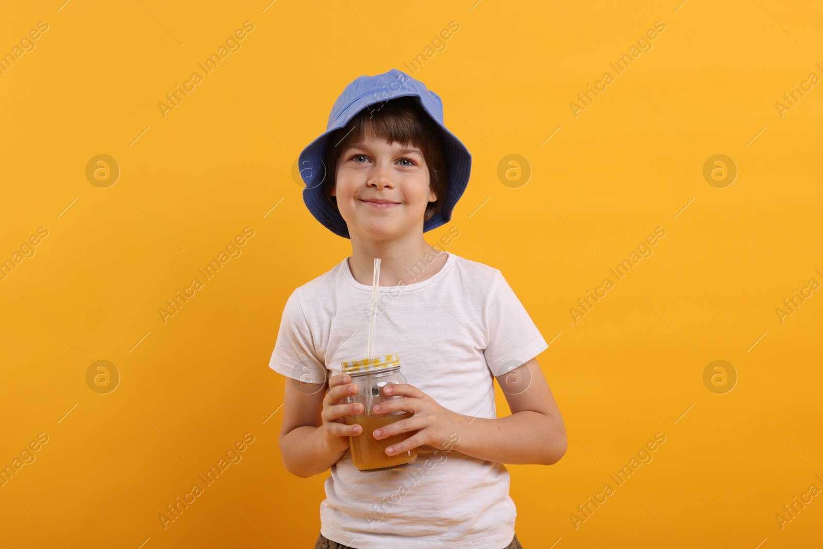 Cute little boy in panama hat with mason jar of juice on orange background. Refreshing drink Photo of Cute little boy in panama hat with mason jar of juice on orange background. Refreshing drink