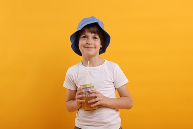 Photo of Cute little boy in panama hat with mason jar of juice on orange background. Refreshing drink