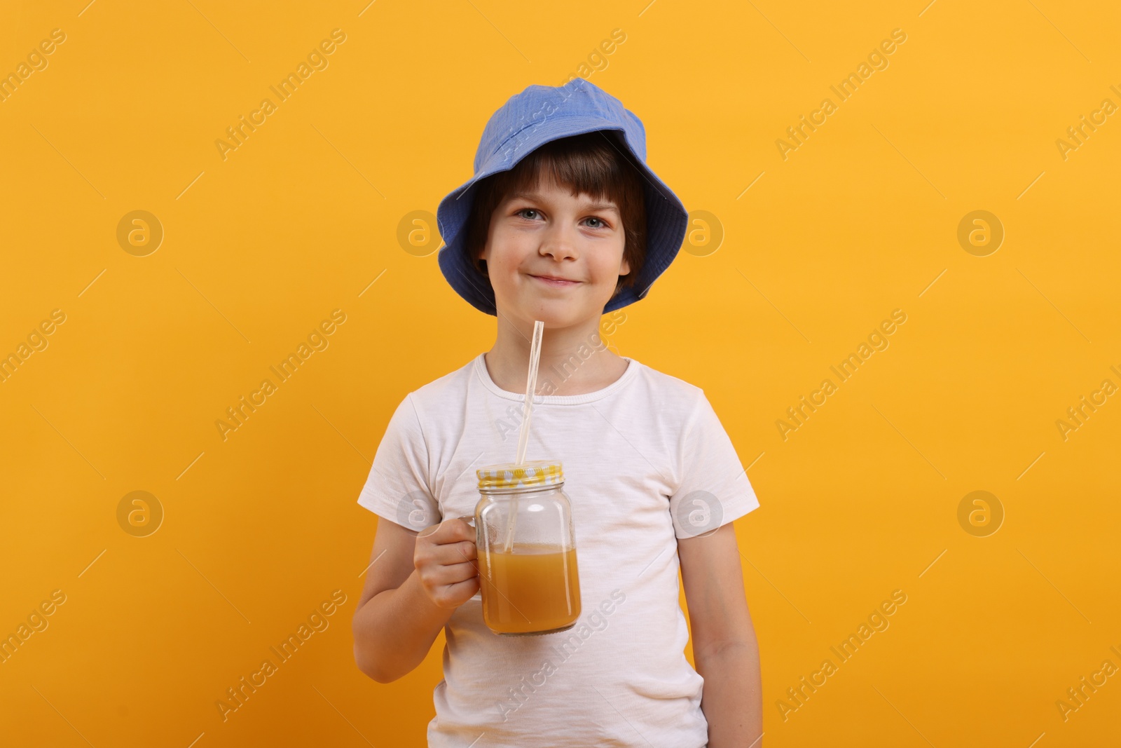 Cute little boy in panama hat with mason jar of juice on orange background. Refreshing drink Photo of Cute little boy in panama hat with mason jar of juice on orange background. Refreshing drink