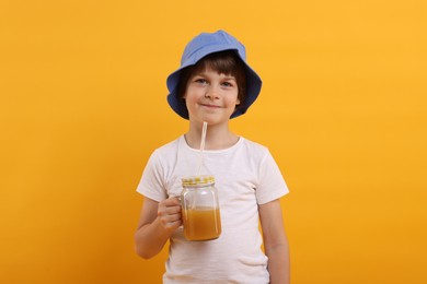 Photo of Cute little boy in panama hat with mason jar of juice on orange background. Refreshing drink