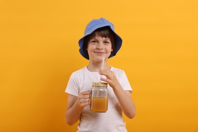 Photo of Cute little boy in panama hat with mason jar of juice on orange background. Refreshing drink