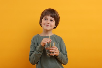 Photo of Cute little boy with glass of refreshing soda drink on orange background