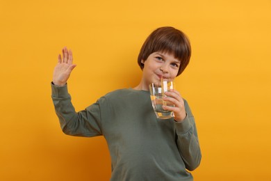 Photo of Cute little boy drinking refreshing soda on orange background