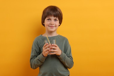 Photo of Cute little boy with glass of refreshing soda drink on orange background