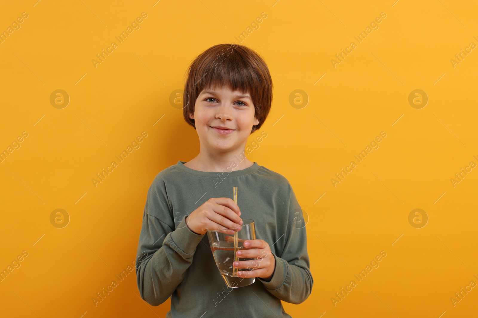 Cute little boy with glass of refreshing soda drink on orange background Photo of Cute little boy with glass of refreshing soda drink on orange background