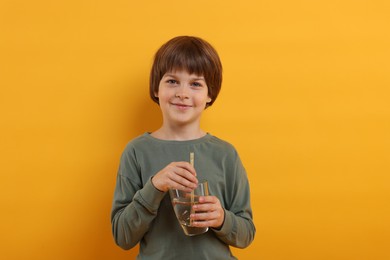Photo of Cute little boy with glass of refreshing soda drink on orange background