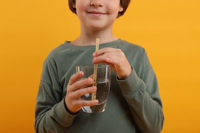Photo of Little boy with glass of refreshing soda drink on orange background, closeup