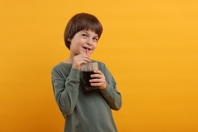 Photo of Cute little boy drinking refreshing soda on orange background