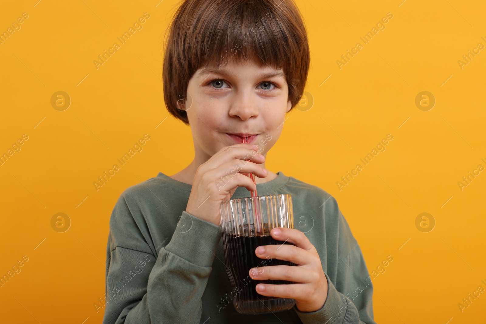 Cute little boy drinking refreshing soda on orange background Photo of Cute little boy drinking refreshing soda on orange background