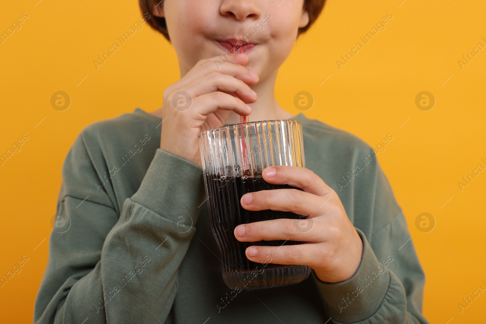 Little boy drinking refreshing soda on orange background, closeup Photo of Little boy drinking refreshing soda on orange background, closeup