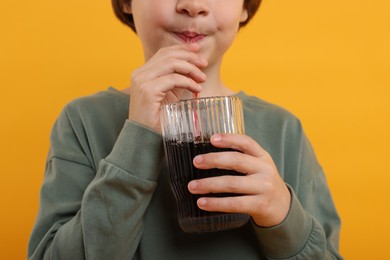 Photo of Little boy drinking refreshing soda on orange background, closeup