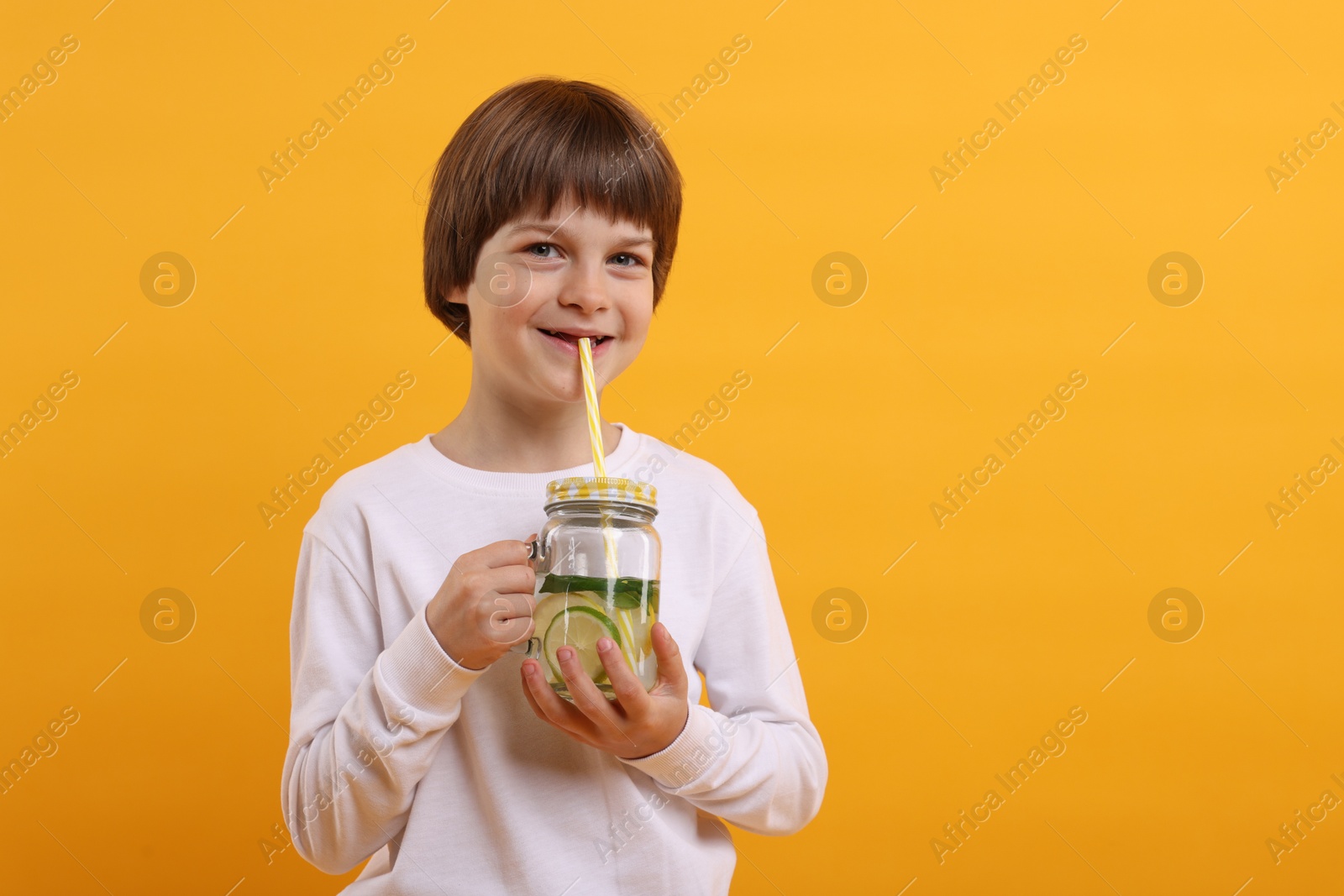 Cute little boy drinking lemonade on orange background, space for text. Refreshing drink Photo of Cute little boy drinking lemonade on orange background, space for text. Refreshing drink