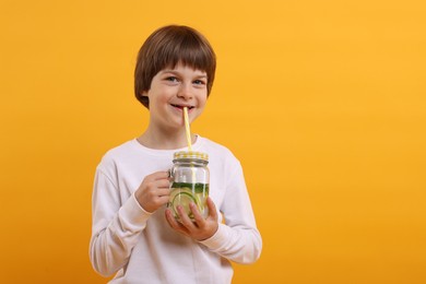 Photo of Cute little boy drinking lemonade on orange background, space for text. Refreshing drink
