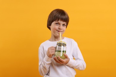 Photo of Cute little boy drinking lemonade on orange background. Refreshing drink