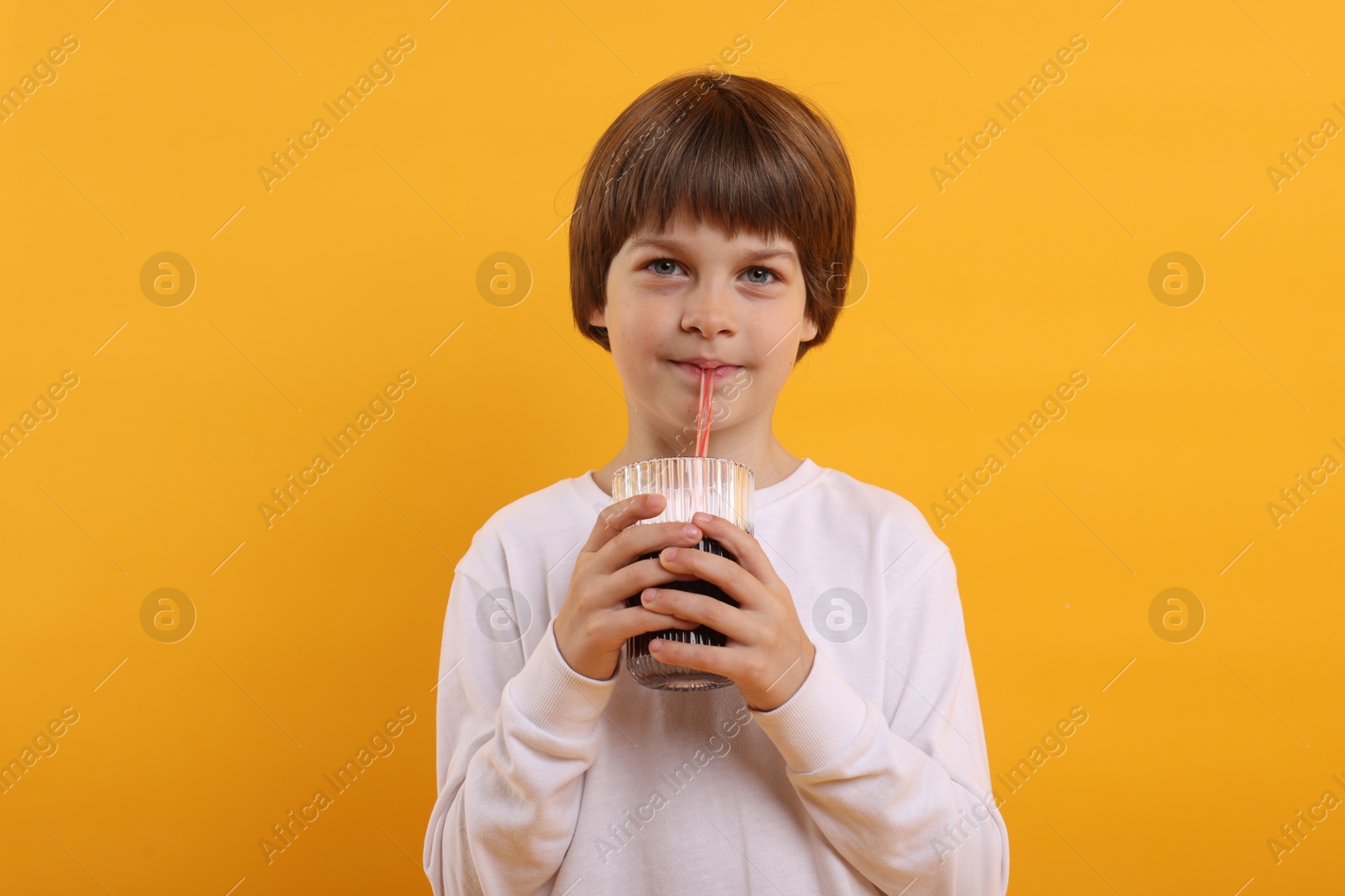 Cute little boy drinking refreshing soda on orange background Photo of Cute little boy drinking refreshing soda on orange background