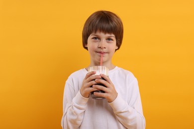 Photo of Cute little boy drinking refreshing soda on orange background