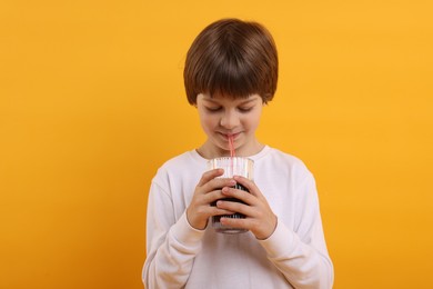 Photo of Cute little boy drinking refreshing soda on orange background