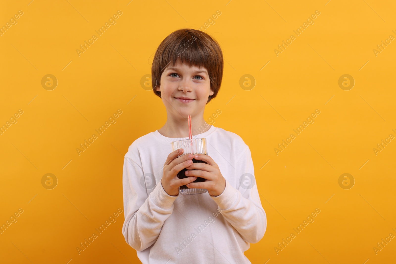 Cute little boy with glass of refreshing soda drink on orange background Photo of Cute little boy with glass of refreshing soda drink on orange background