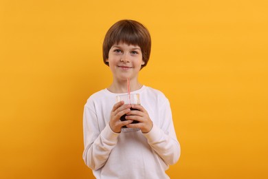 Photo of Cute little boy with glass of refreshing soda drink on orange background