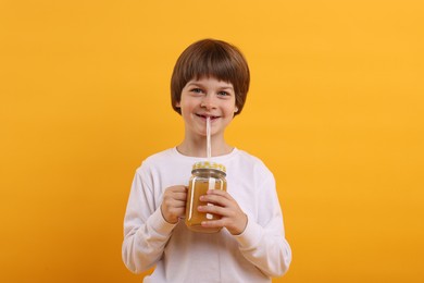 Photo of Happy little boy drinking juice on orange background. Refreshing drink