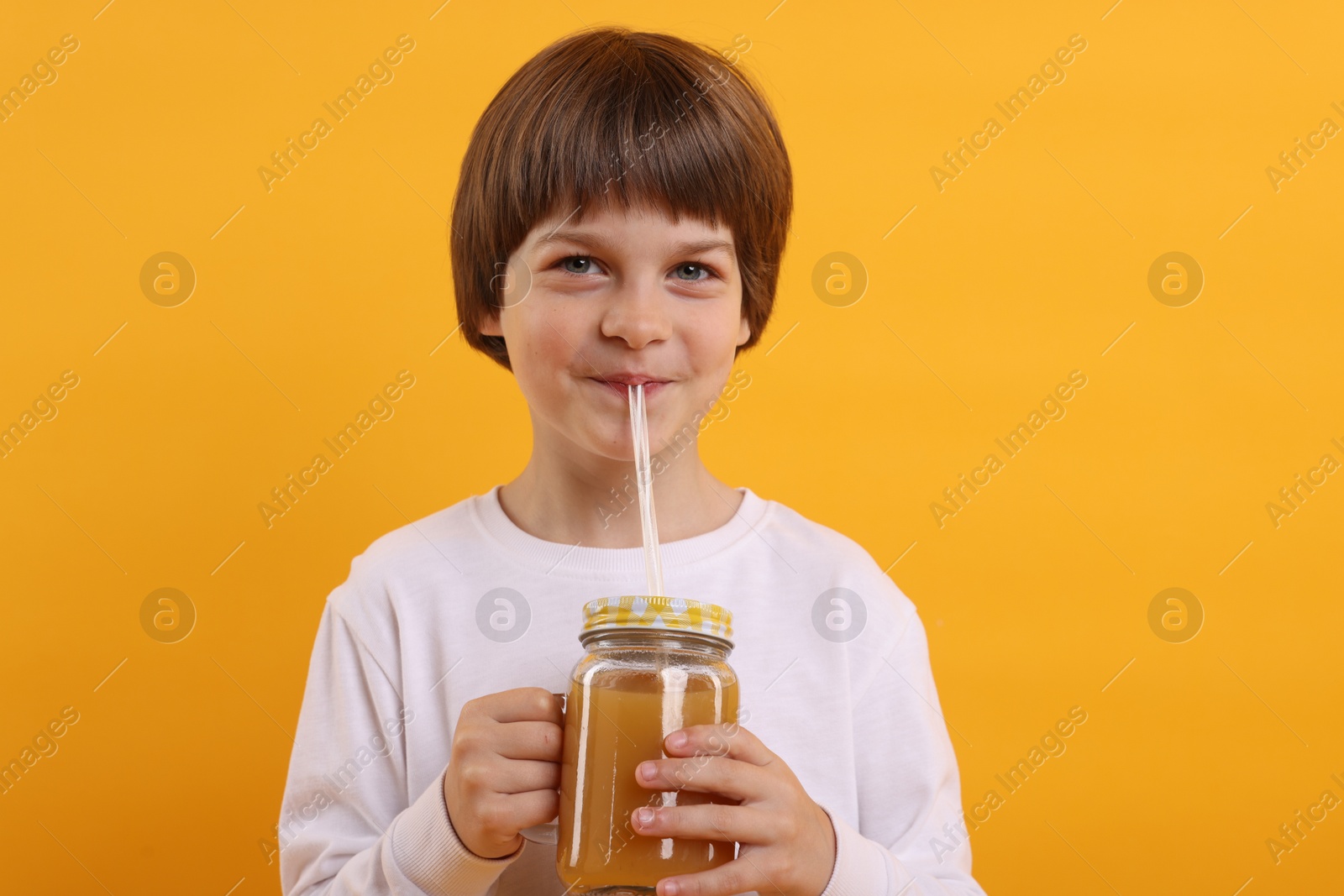 Cute little boy drinking juice on orange background. Refreshing drink Photo of Cute little boy drinking juice on orange background. Refreshing drink