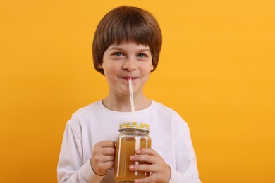 Photo of Cute little boy drinking juice on orange background. Refreshing drink