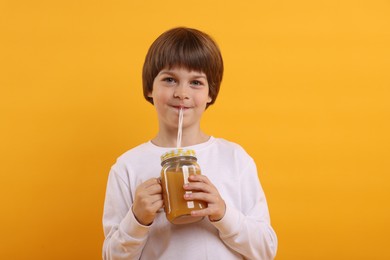 Photo of Cute little boy drinking juice on orange background. Refreshing drink