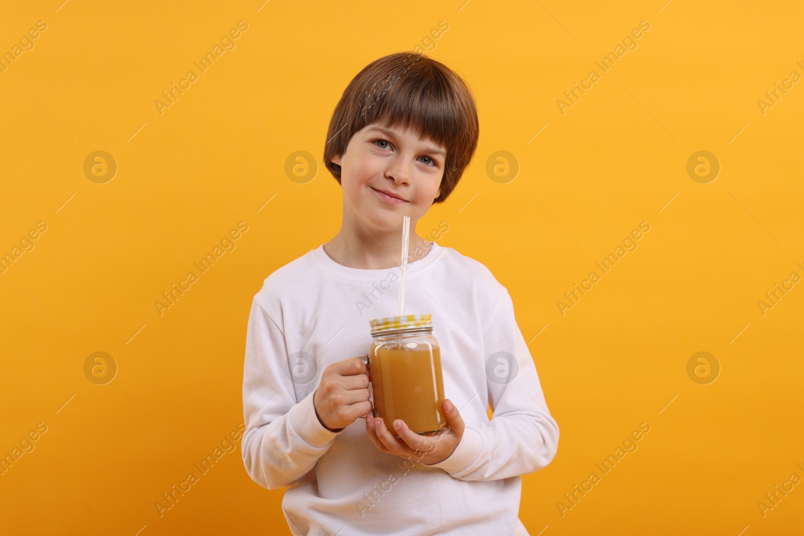 Cute little boy with mason jar of juice on orange background. Refreshing drink Photo of Cute little boy with mason jar of juice on orange background. Refreshing drink