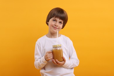 Photo of Cute little boy with mason jar of juice on orange background. Refreshing drink