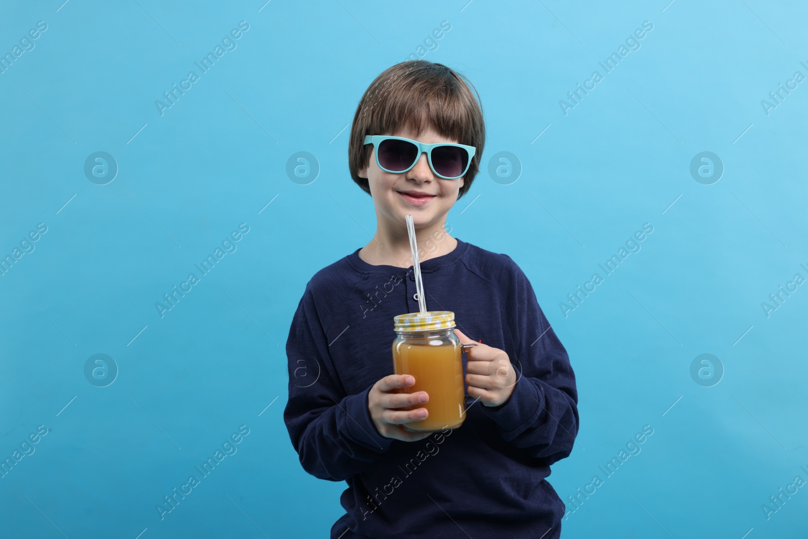 Happy little boy in sunglasses with mason jar of orange juice on light blue background. Refreshing drink Photo of Happy little boy in sunglasses with mason jar of orange juice on light blue background. Refreshing drink