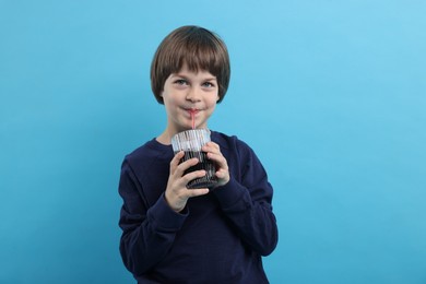 Photo of Cute little boy drinking refreshing soda on light blue background