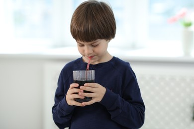 Photo of Cute little boy drinking refreshing soda at home
