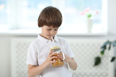 Photo of Cute little boy drinking orange juice at home. Refreshing drink