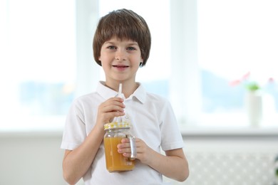 Photo of Cute little boy with mason jar of orange juice at home. Refreshing drink