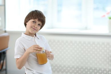 Photo of Cute little boy with mason jar of orange juice at home, space for text. Refreshing drink