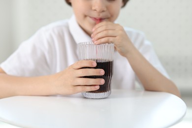 Photo of Little boy drinking refreshing soda at table indoors, closeup