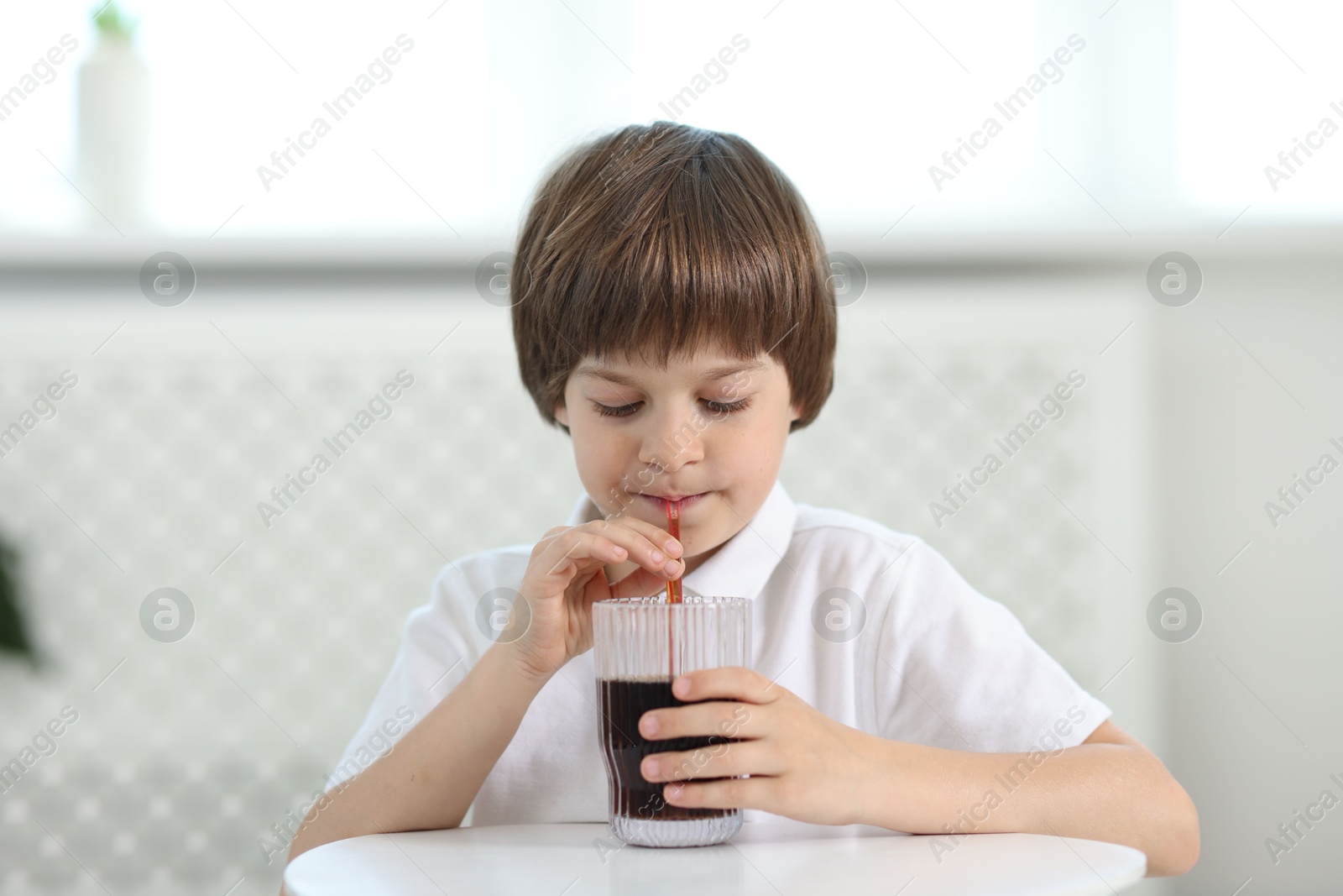 Cute little boy drinking refreshing soda at table indoors Photo of Cute little boy drinking refreshing soda at table indoors