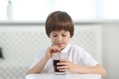 Photo of Cute little boy drinking refreshing soda at table indoors