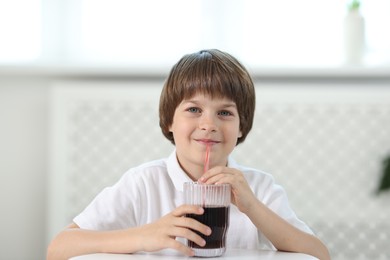 Photo of Cute little boy drinking refreshing soda at table indoors