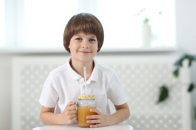 Photo of Little boy with mason jar of orange juice at table indoors. Refreshing drink