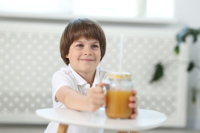 Photo of Little boy with mason jar of orange juice at table indoors, selective focus. Refreshing drink