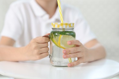 Photo of Little boy with mason jar of lemonade at table indoors, selective focus. Refreshing drink
