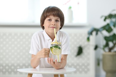 Photo of Cute little boy drinking lemonade at table indoors. Refreshing drink