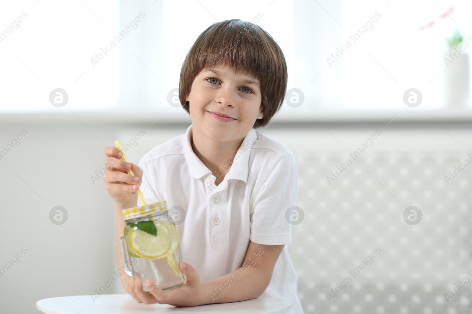Cute little boy with mason jar of lemonade at table indoors. Refreshing drink Photo of Cute little boy with mason jar of lemonade at table indoors. Refreshing drink
